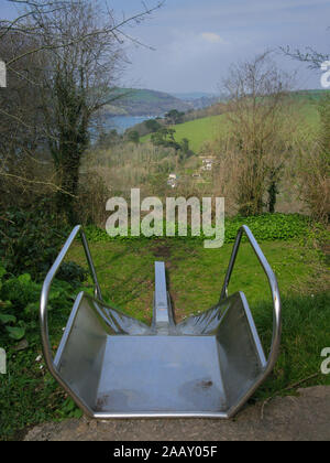 Eine Ansicht von einer Folie. Kinder leer Rutschbahn mit Blick über die grünen Felder und den Fluss Dart, in der Nähe von Dartmouth, Devon Stockfoto