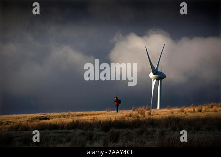 Walker auf dem Hügelkamm, der von Windturbinen mit dramatischem Himmel am späten Nachmittag in den South Wales Valleys in den Schatten gestellt wurde. Stockfoto