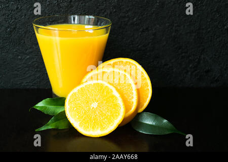 Glas orange und Orangenscheiben auf schwarzem Hintergrund. Stockfoto