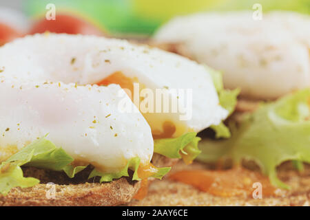 Pochiertes Ei mit einer Kerbe Nahaufnahme, Salat und Tomaten auf dem Hintergrund. Stockfoto