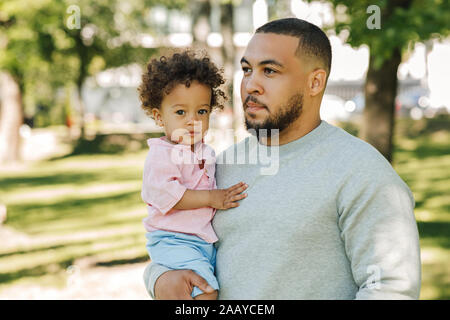 Portrait einer jungen Eltern sein kleiner Sohn in Händen hält. Cute curly Boy mit Blick auf die Kamera in den Park. Stockfoto