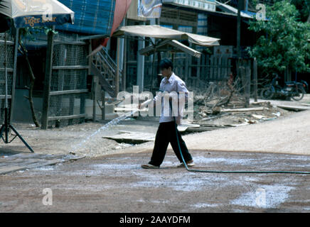 Eine indigene Kreung mann Sprays der Schmutz der Straße in seinem Dorf den Staub an der Bucht zu halten. Provinz Ratanakiri, canbodia. Stockfoto