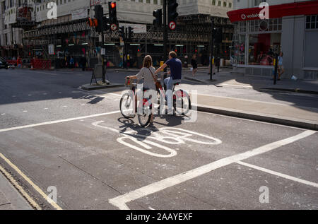 Zwei Radfahrer Männer und Frauen warten auf einen Fahrradweg Ampelkreuzung auf Sharing Autovermietung Santander Zyklen. Stockfoto