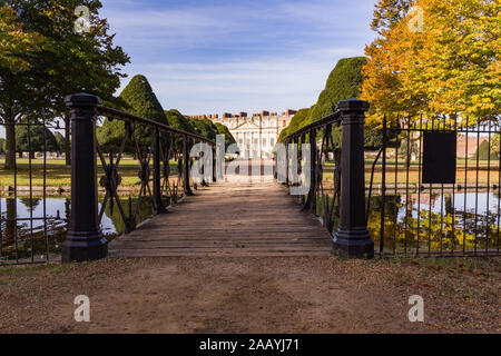 Georgianische Fassade der Hampton Court Palace gesehen aus über eine Brücke über einen Teich von schmiedeeisernen Geländer und eine Linie von Eiben an einem sonnigen grenzt d Stockfoto