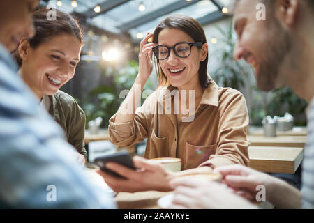 Porträt der moderne junge Frau am Bildschirm des Smartphones suchen und lächelnd, während sie das Mittagessen mit Freunden im Cafe Stockfoto