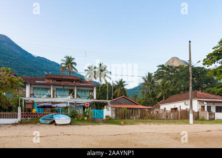 Ilha Grande, Brasilien. 24. Dezember, 2012. Strandpromenade, Hostel mit Booten auf sandigen Strand während der sonnigen Morgen im Vila tun sehen Santorini Santorini (Dorf), Ilha Grande, die Gemeinde von Angra dos Reis, Bundesstaat Rio de Janeiro, Brasilien. Am 5. Juli 2019, Ilha Grande wurde von der UNESCO als Weltkulturerbe eingetragen. Stockfoto