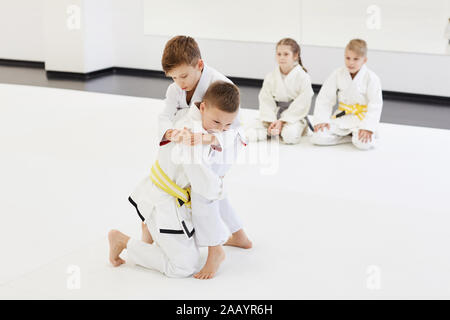 Zwei Jungen kämpfen, während andere Kinder sitzen auf dem Boden und Sie während der Konkurrenz im Karate Stockfoto