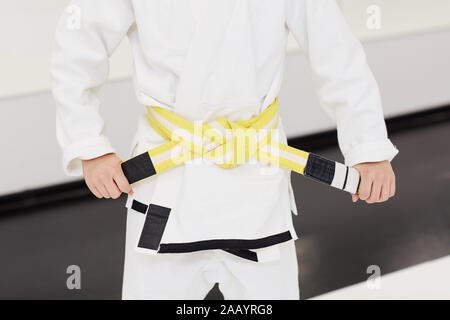 In der Nähe des kleinen Jungen im weissen Kimono und tieing den gelben Gürtel auf seine Taille vor dem Training im Karate Stockfoto