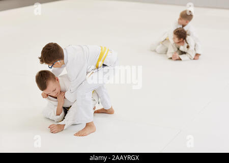 Jungen miteinander kämpfen auf dem Boden mit Jungen und Mädchen kämpfen miteinander im Hintergrund, während Sie im Training im Karate Stockfoto