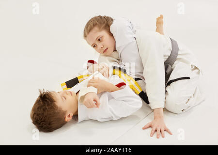 Mädchen und Jungen im Kimono Kampf mit jedem anderen auf dem Boden während der Ausbildung in Karate Stockfoto