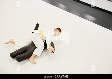 Junge judoist auf dem Boden liegen und Training mit Mannequin während der Lektion im Karate in der Turnhalle Stockfoto