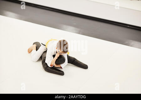 Kleiner Junge im Kimono auf dem Boden liegen und kämpfen mit Mannequin während des Trainings im Judo Stockfoto