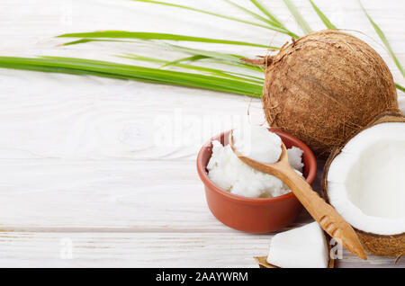 Hintergrund der Kokosnuss, Kokosnussschalen, Öl in Ton Schüssel und Löffel auf weiße Holztisch Stockfoto