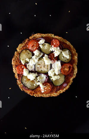 Gesund Glutenfreie keto Essen. Blumenkohl Pizza mit Auberginen, Tomaten, Ziegenkäse und Sesam auf schwarzem Hintergrund oben Ansichtskopie Raum Stockfoto