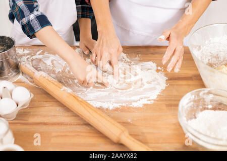 Hände von Mutter und Sohn Zeichnung auf hölzernen Tisch mit Mehl beim Gehen zum Kneten von Teig und stellen Cookies oder andere Gebäck Stockfoto