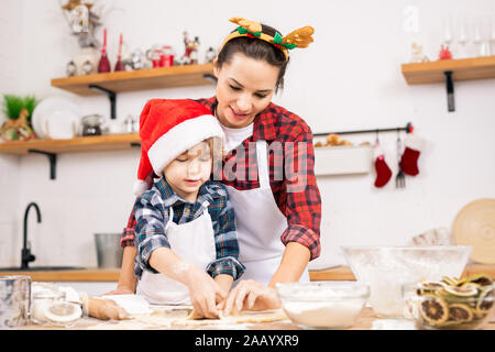 Cute little boy in Santa Cap und seine Mutter in Weihnachten Stirnband, Gingerbread Cookies in der Küche Stockfoto