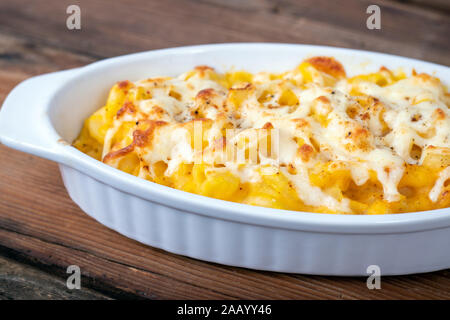 Butternut-kürbis Mac und Käse Teller closeup auf rustikalem Tisch und geriebenen Käse auf der Oberseite Stockfoto