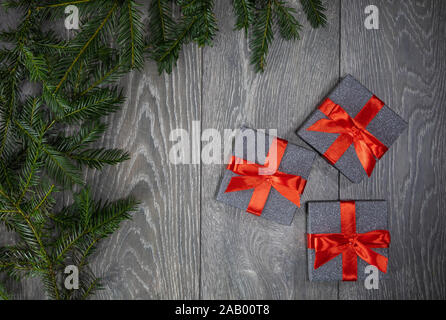 Drei Weihnachten Geschenke Kartons auf einer grauen Holzboden Hintergrund und der Niederlassung von einem Weihnachtsbaum grenzt an der linken Seite der Fotografie Stockfoto