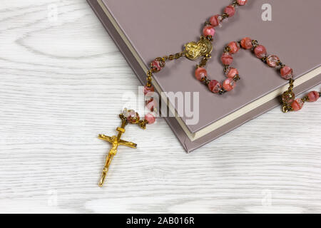 Rosenkranz mit rosa gefärbte Körner liegen auf einem Buch auf einem weißen Tisch Stockfoto