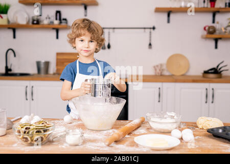 Cute little boy Sichten Mehl über Schüssel beim Gehen Teig für hausgemachte Kuchen in der Küche zu machen Stockfoto