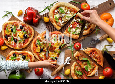 Vegetarische Familie Mahlzeit. Frau und Kind Hände greifen für Pizza Scheiben mit Oliven und Gemüse auf weißem Hintergrund der Ansicht von oben Stockfoto