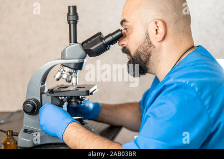 Männliche Laboratory Assistant Prüfung biomaterial Proben in einem Mikroskop. Stockfoto