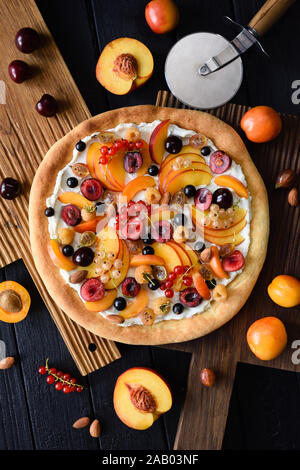 Hausgemachten gesunden Nachtisch. Obst Pizza mit raw Pfirsiche, Aprikosen, Kirschen, Johannisbeeren und Himbeeren mit Ricotta Zuckerguß auf dunklen Eiche Top View Stockfoto