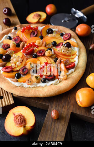 Gesunder Nachtisch. Obst, hausgemachte Pizza mit rohen Pfirsiche, Aprikosen, Kirschen, Johannisbeeren und Ricotta Creme auf dunklem Hintergrund hohen Winkel anzeigen Stockfoto