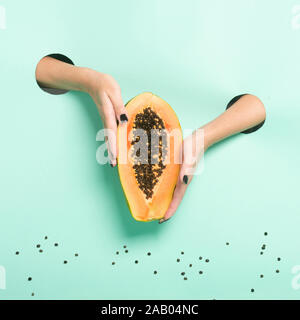 Weibliche Hände halten frischer Papaya durch ein Loch auf Neon mint Hintergrund. Stockfoto