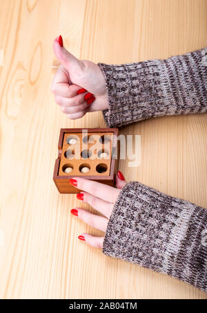 Das Mädchen hob ihre Daumen hoch, nach dem Zusammenbau der Puzzle. Holzpuzzle Kugeln und Bohrungen. Helle Maniküre auf Fingernägeln. Puzzle Konzept. Stockfoto