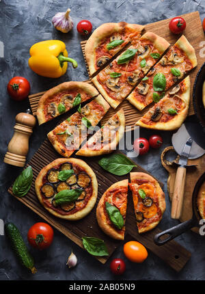 Flatlay vegetarische Pizza Party. Hausgemachte rustikale Pizza mit Tomaten, Pilzen, Paprika, Auberginen und Basilikum auf dunklem Hintergrund, Ansicht von oben Stockfoto