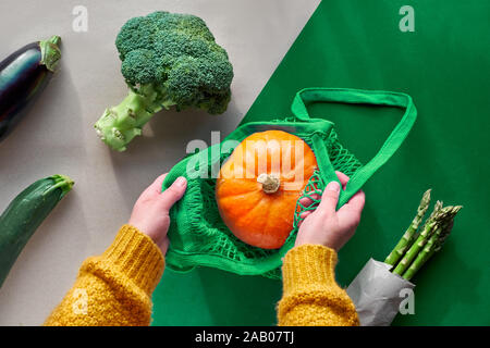 Umweltfreundliche null Abfall flach mit Hände halten Brokkoli und String Tasche mit orange Kürbis. Herbst oder Frühjahr Draufsicht von oben mit Gemüse o Stockfoto