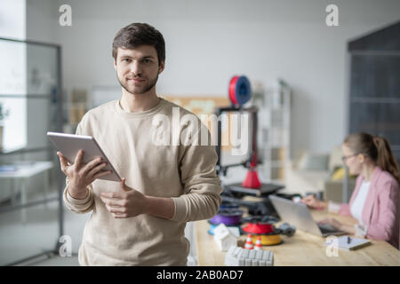 Geschäftsmann mit Touchpad auf dem Hintergrund der Kollegen arbeiten mit 3d-Drucker Stockfoto