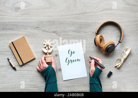 Konzept null Abfall bewussten Konsum Flach, Blick von Oben auf die Hände, die trendigen Holz- Blume und Marker. Text "Go Green", Handwerk moleskin Notebook Stockfoto