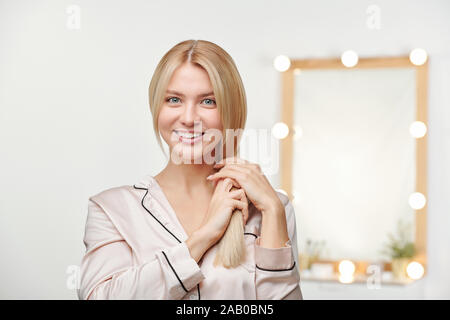 Ziemlich lächelnd weibliche in seidenpyjama Ihren langen blonden Haar Holding Stockfoto