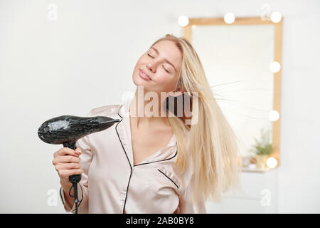 Junge schöne Frau, die Freude an der warmen Luft während Sie Haartrockner Stockfoto