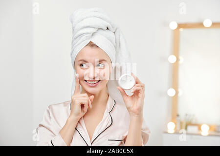 Frische junge schöne Frau mit weißen Handtuch auf dem Kopf ihre Gesichtscreme auftragen Stockfoto