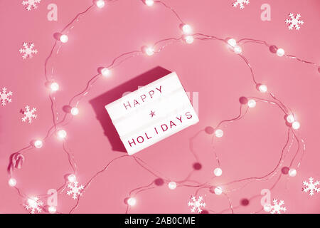 Lightbox mit Text 'Happy Holidays' auf Coral Farbe oder pink festliche Papier Hintergrund mit Girlande von glänzenden runden Leuchten. Frohe Weihnachten und einen guten Rutsch ins Ne Stockfoto