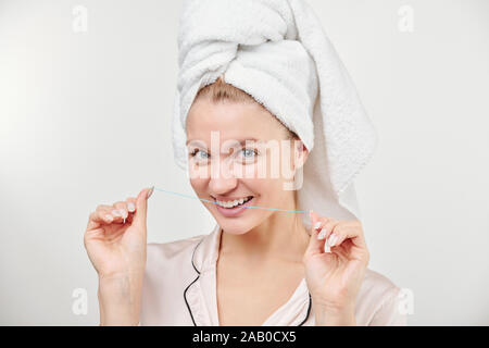 Freundliche gesunde junge Frau mit Handtuch auf den Kopf ging Zahnseide zu verwenden Stockfoto