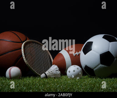 Sportgeräte, Schläger und Bälle auf grünem Gras mit schwarzem Hintergrund und Kopieren. Stockfoto