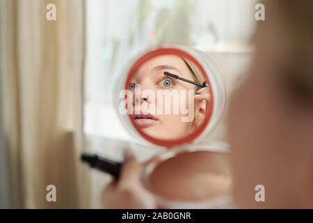 Reflexion im Spiegel der jungen Frau, die schwarze Mascara auf die Wimpern Stockfoto