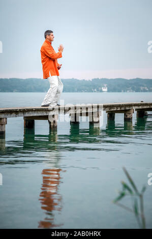 Ein Mann, der am fruehen Morgen Qi-Gong-Uebungen am Starnberger See durchfuehrt Stockfoto