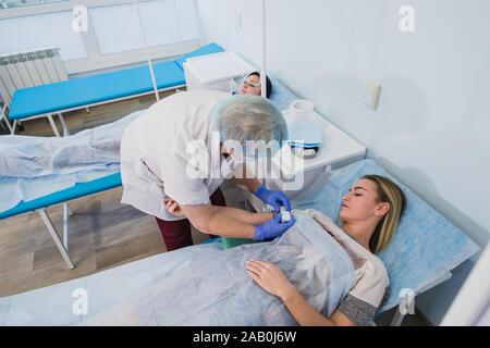 Krankenschwester macht eine Injektion mit einer Frau am OP-Tisch am Klinikum Vorbereitung Narkose medizinische Arztpraxis Konzept liegen. Stockfoto