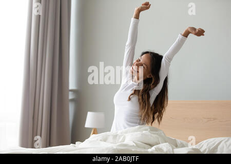 Frau sitzt im Bett strecken ihre Arme Muskeln nach Schlaf Stockfoto