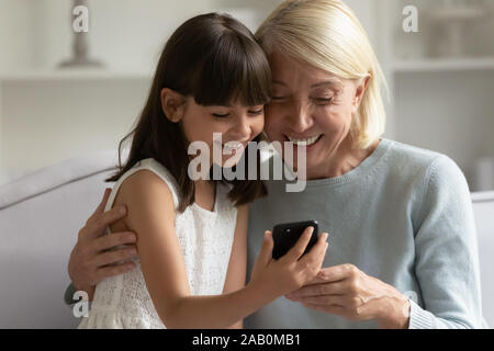 Schöne kleine Enkelin Spaß mit Großmutter mit Smartphone App Stockfoto