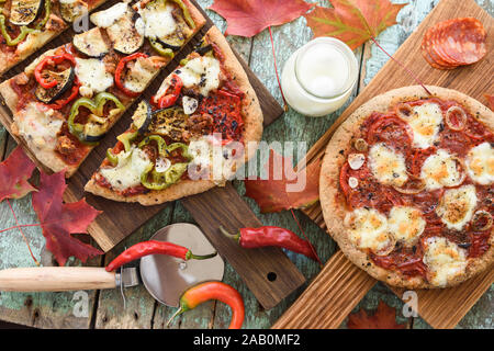 Komfort Essen. Hausgemachte Pizza mit Auberginen, Paprika, Salami und Mozarella auf Eiche mit rohen Zutaten mit Ahorn Blätter oben serviert Stockfoto