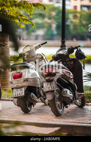 Hanoi, Vietnam - 11. Oktober 2019: Zwei Motorroller stehen in einer Zeile in Hanoi vor einem großen See an einem sonnigen Tag. Stockfoto