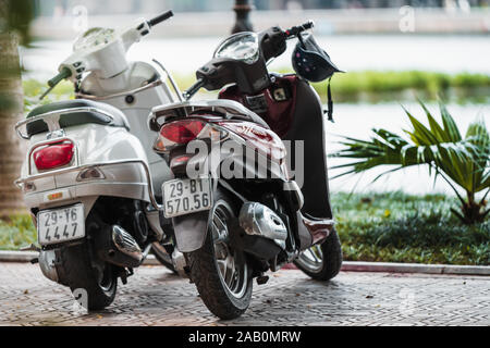 Hanoi, Vietnam - 11. Oktober 2019: Zwei Motorroller stehen in einer Zeile in Hanoi vor einem großen See an einem sonnigen Tag. Stockfoto