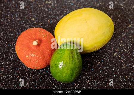 Bunte runde Gemüse und Früchte auf dunklem Hintergrund. Kürbis, Melone und Avocado noch leben. Farbe einfache abstrakte Komposition. Food Art Konzept Stockfoto