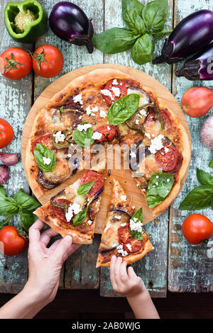 Leckere hausgemachte rustikale Pizza. Frau und Baby Hände greifen für Stücke von auberginen Pizza mit Ricotta und Basilikum Draufsicht Stockfoto